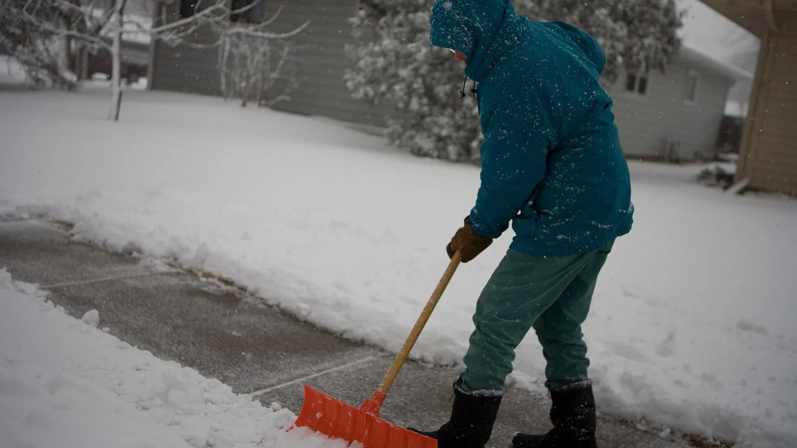 Anwohner räumt bei Schneefall den Gehweg vor dem Haus mit der Schneeschaufel
